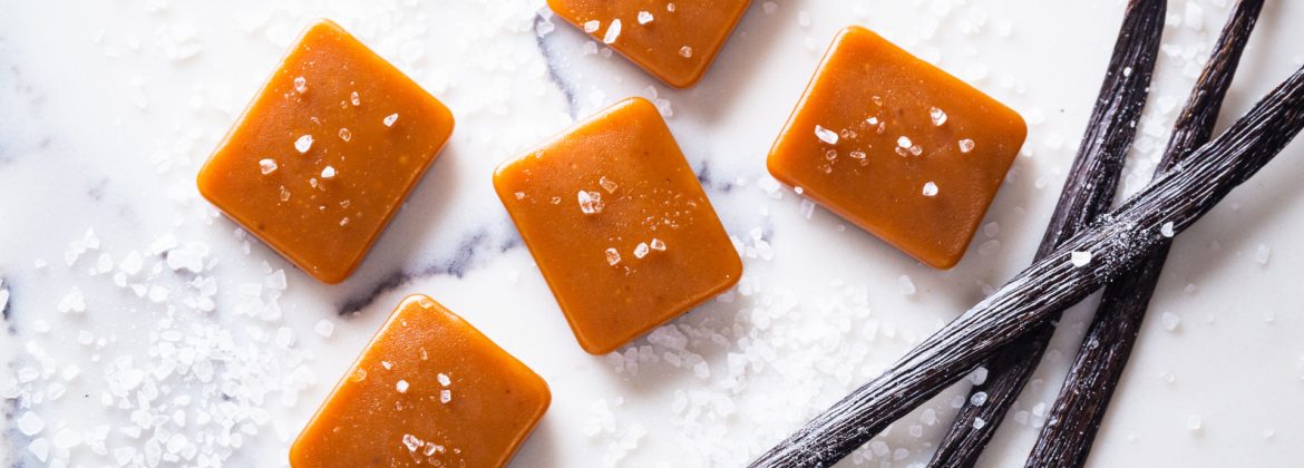 Sira Naturals product image of caramels with seasalt sprinkled on a marble surface and vanilla beans.