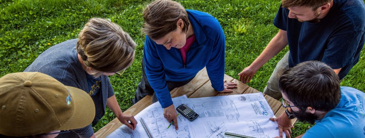 Ecotone design team looking at plans on a picnic table in a grassy area.