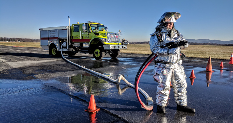 Reading Regional Airport man in a fireproof suit on the runway with a host and truck.