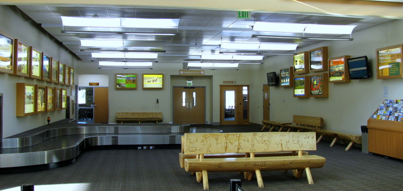 Yellowstone Regional Airport Cody Wyoming, terminal interior showing baggage claim and a wood bench made of logs with carvings in it