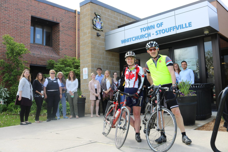 Whitchurch-Stouffville, Ontario bikers and a group of people posing for a group photo outside of a town building.