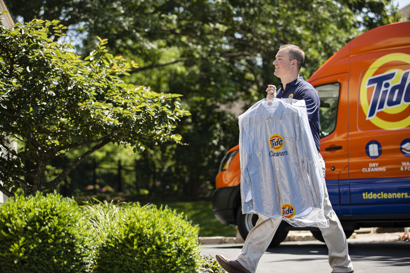 Tide Cleaners. A man walking away from a Tide Cleaners van with clean clothing on a hanger.