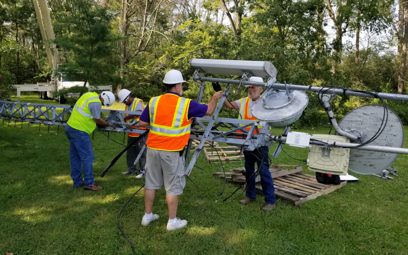 New Lisbon Telephone Company workers working on a tower laying on the ground on its side.