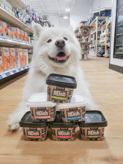 Big Country Raw Side dish products on the floor in a pyramid shape with a dog sitting behind.