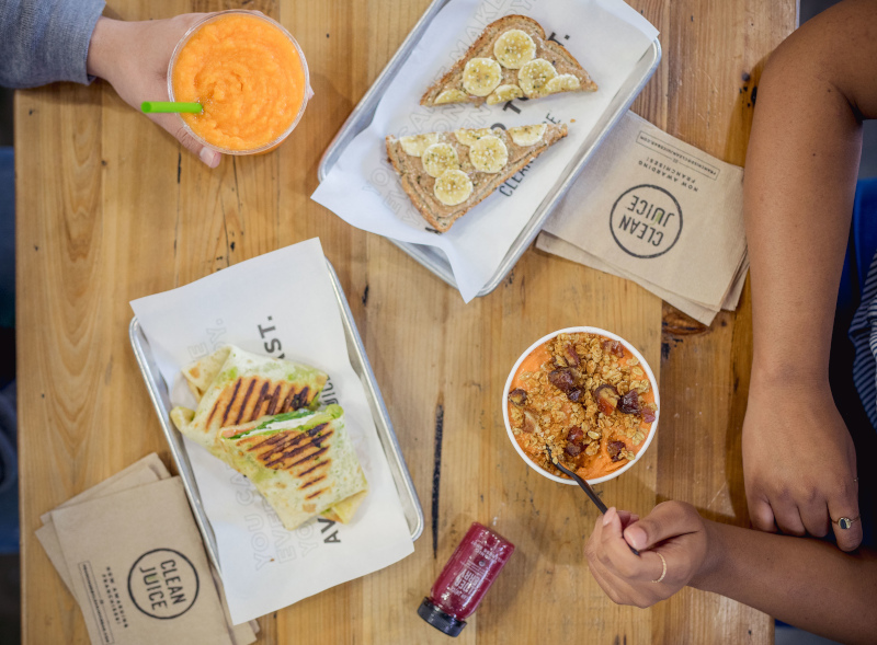 Clean Juice table with the arms showing of people eating food and drink on the table, view from above.