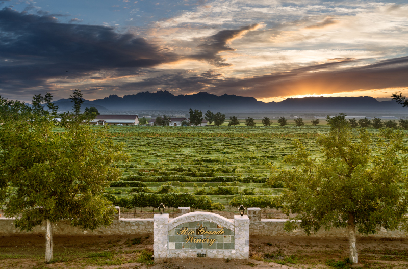 Las Cruces, New Mexico Rio Grande Winery view of landscape with a winery sign in front and mountains and beautiful sky behind.