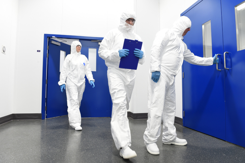 A&C employees in white protective attire entering a room with blue doors.