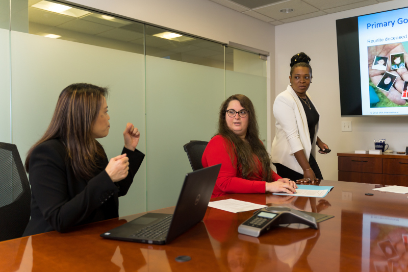 SNA International employees having a meeting at a large table with a monitor on the wall.