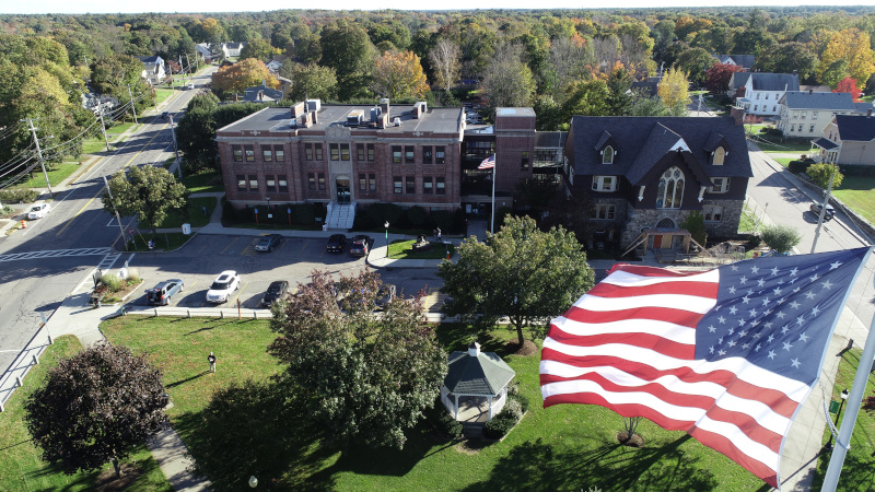 Mansfield, Massachusetts aerial view with US flag in foreground and a building behind.