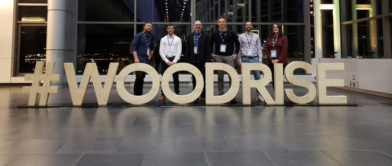 Element5 group of people posing for a photo with a wooden sign in front, saying #woodrise