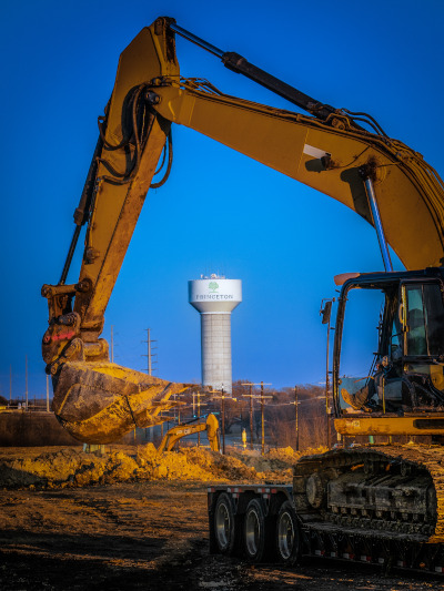 Princeton, Texas excavator with arm curving down, around a water tower the the city name in the distance.